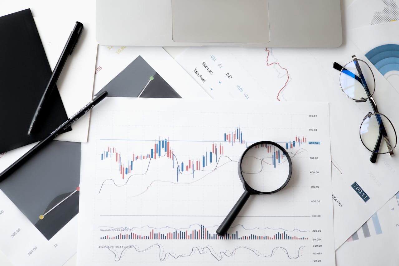 services-04 Flat lay of stock market analysis documents with magnifying glass, pens, and glasses.